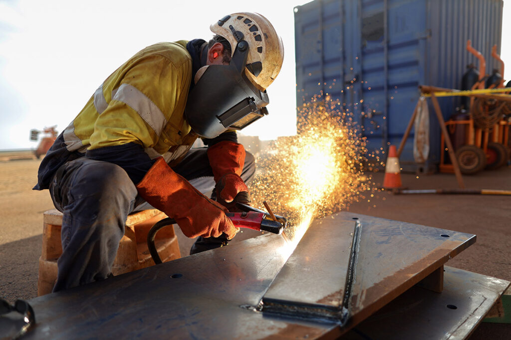 Construction worker wearing a face shield as they weld a piece of carbon steel to a frame.